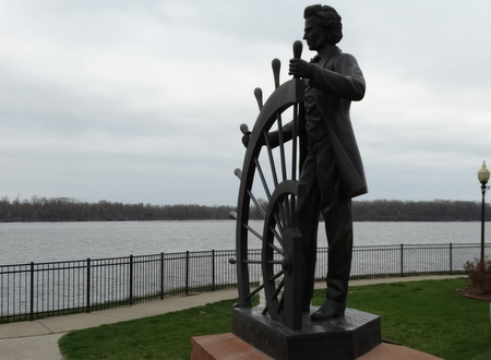 A statue of Mark Twain as a riverboat captain next to the Mississippi River.